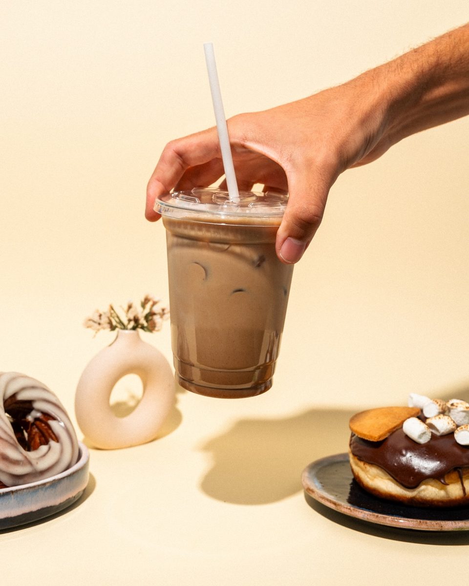 Vasos de café con hielo y donas sobre una superficie crema